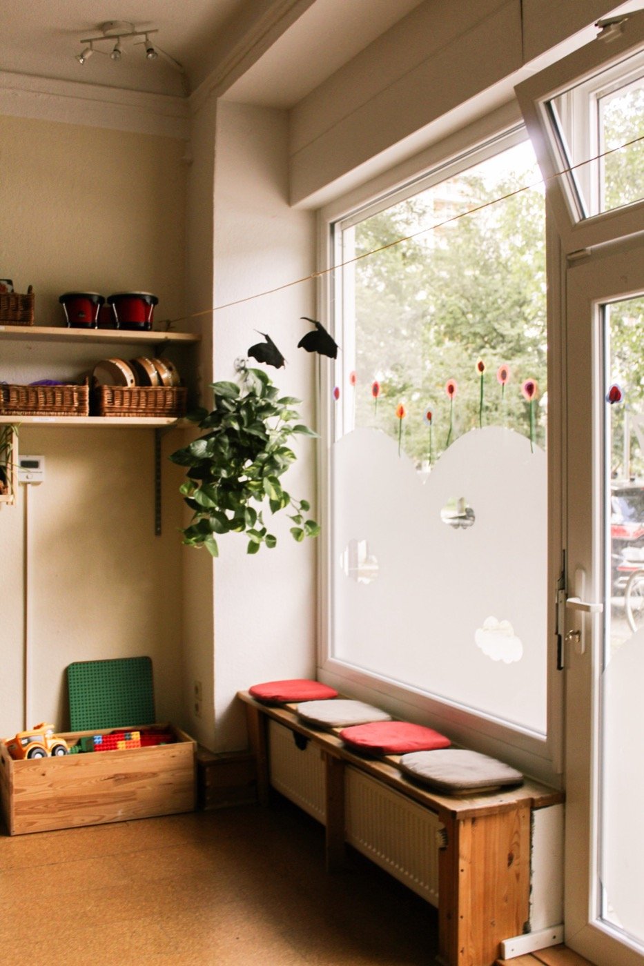 Sonniger Fensterplatz mit Sitzkissen, Pflanze und Spielzeugkisten