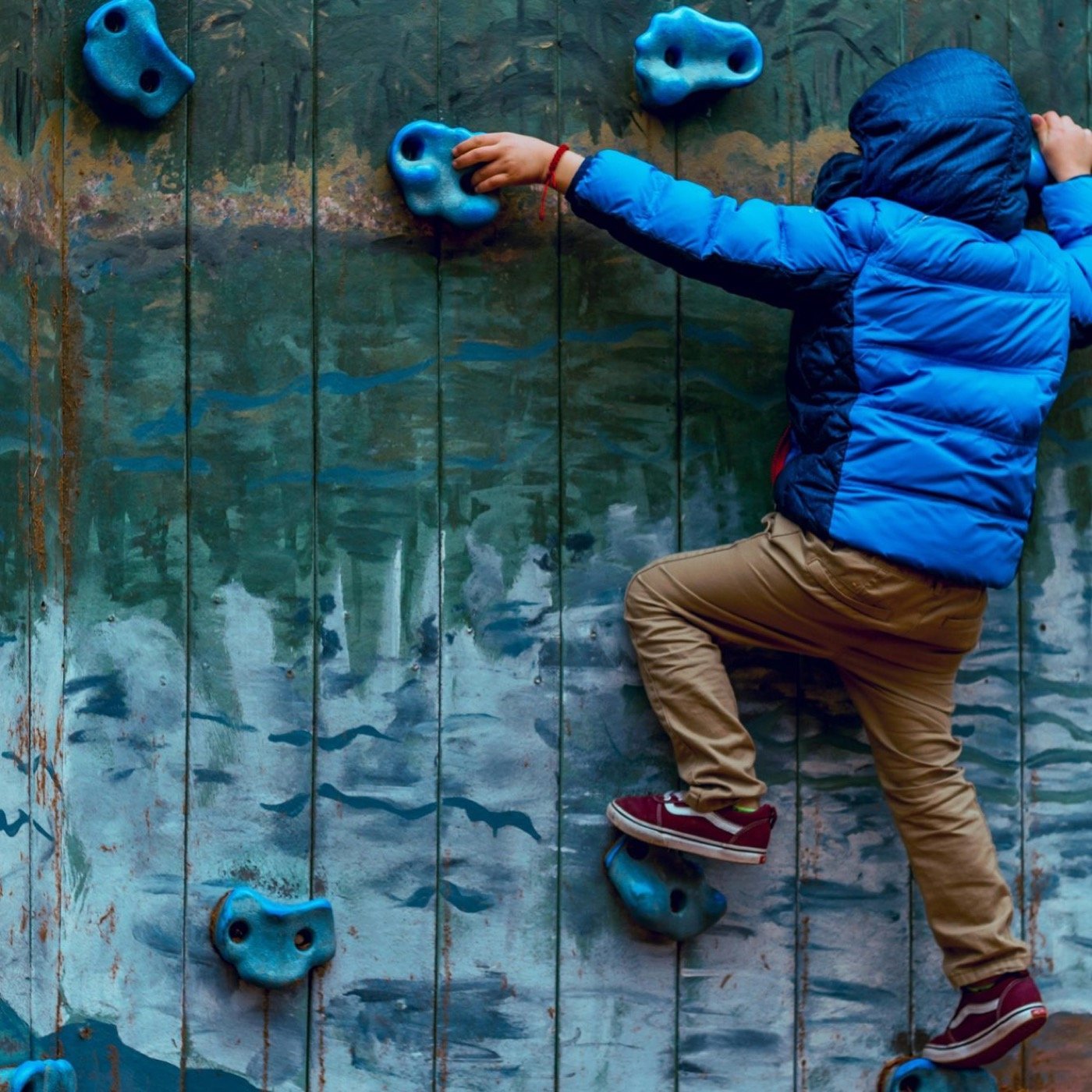 Kind in blauer Jacke klettert an einer Kletterwand