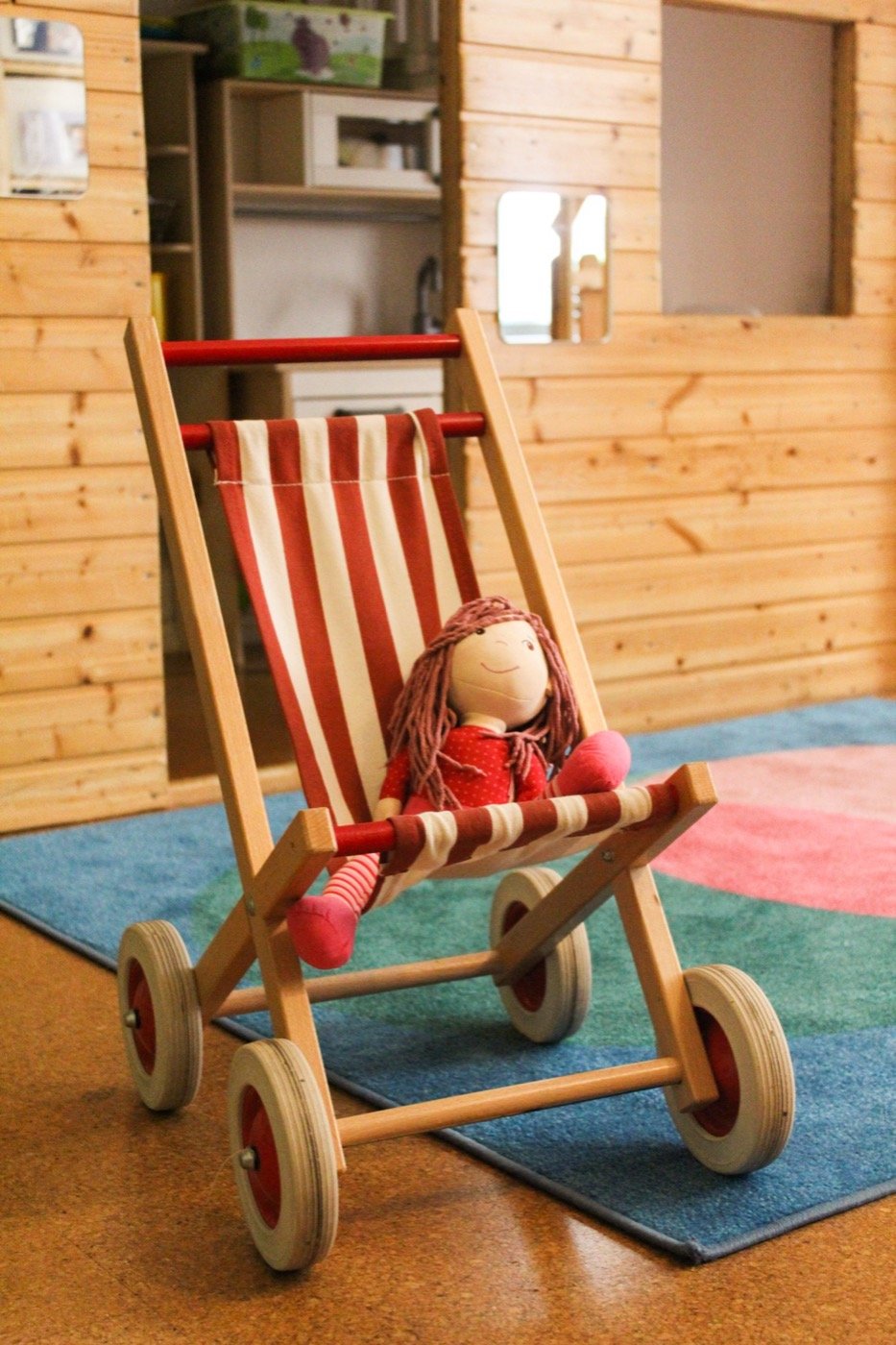 Puppe im Spielzeug-Kinderwagen auf buntem Teppich